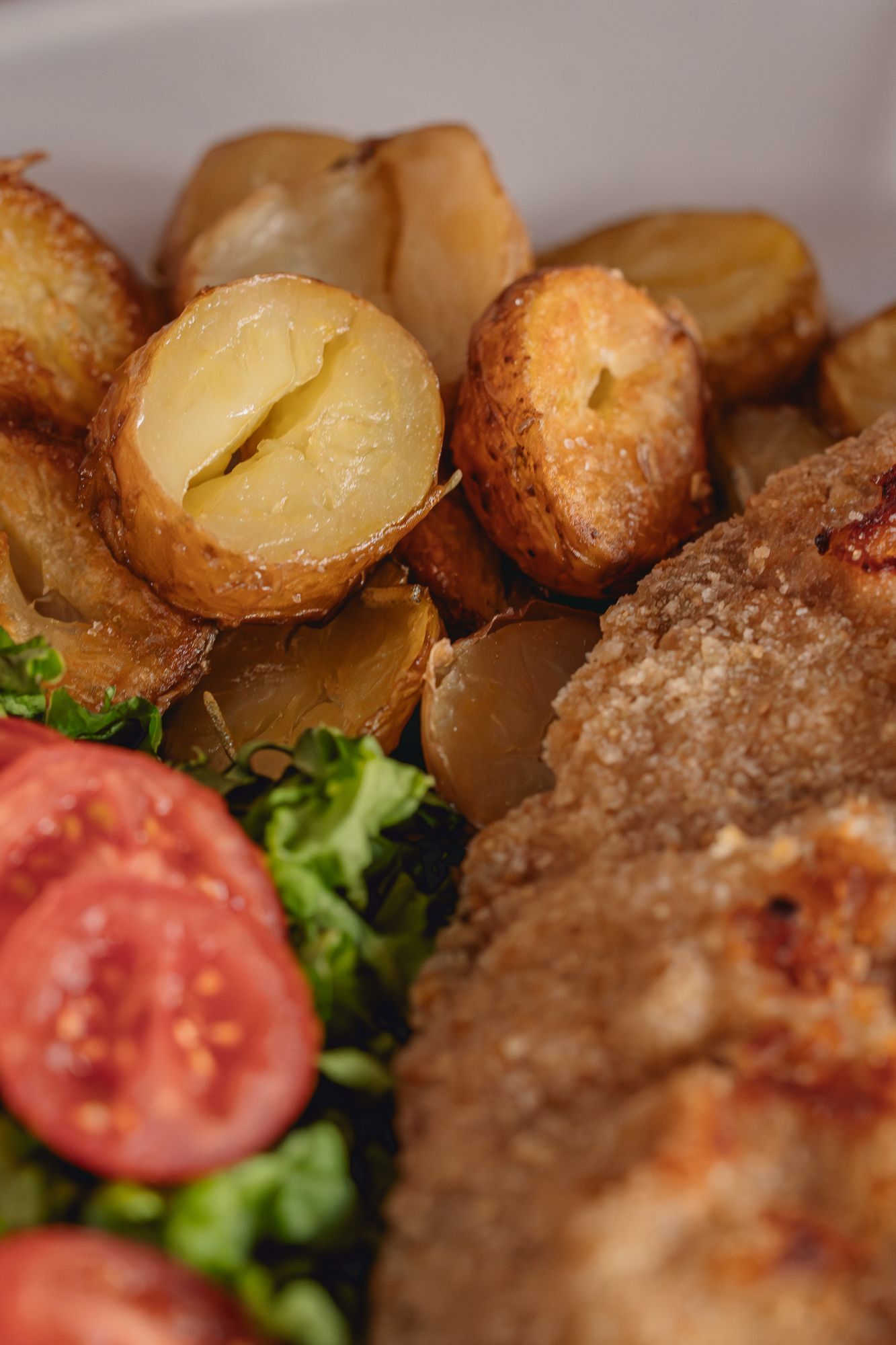 Milanesa de bife de chorizo apanada con pan casero, papas andinas salteadas y mix de verdes